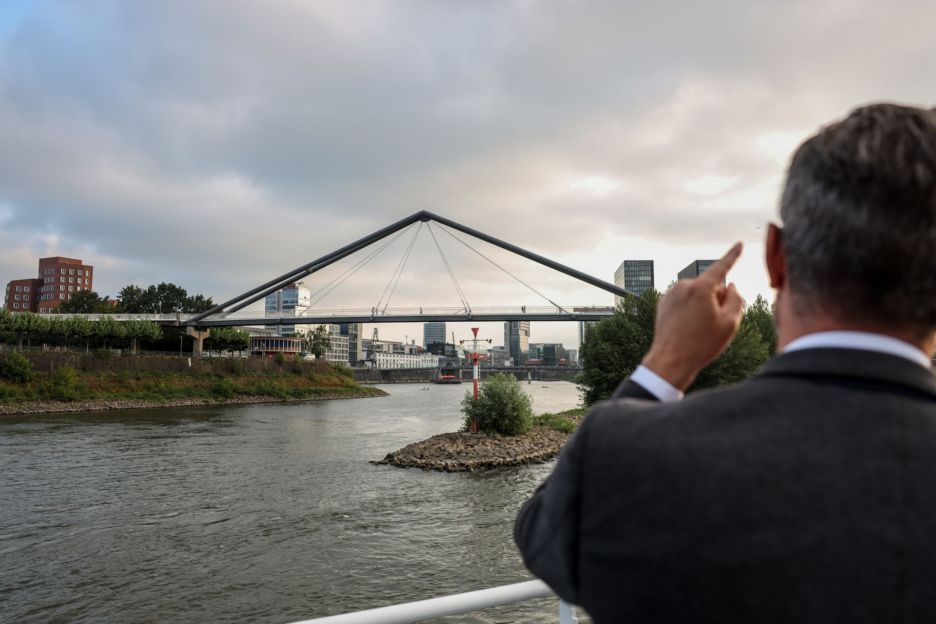 Person with short bob haircut wearing a white pleated-back shirt facing away against a dark background.