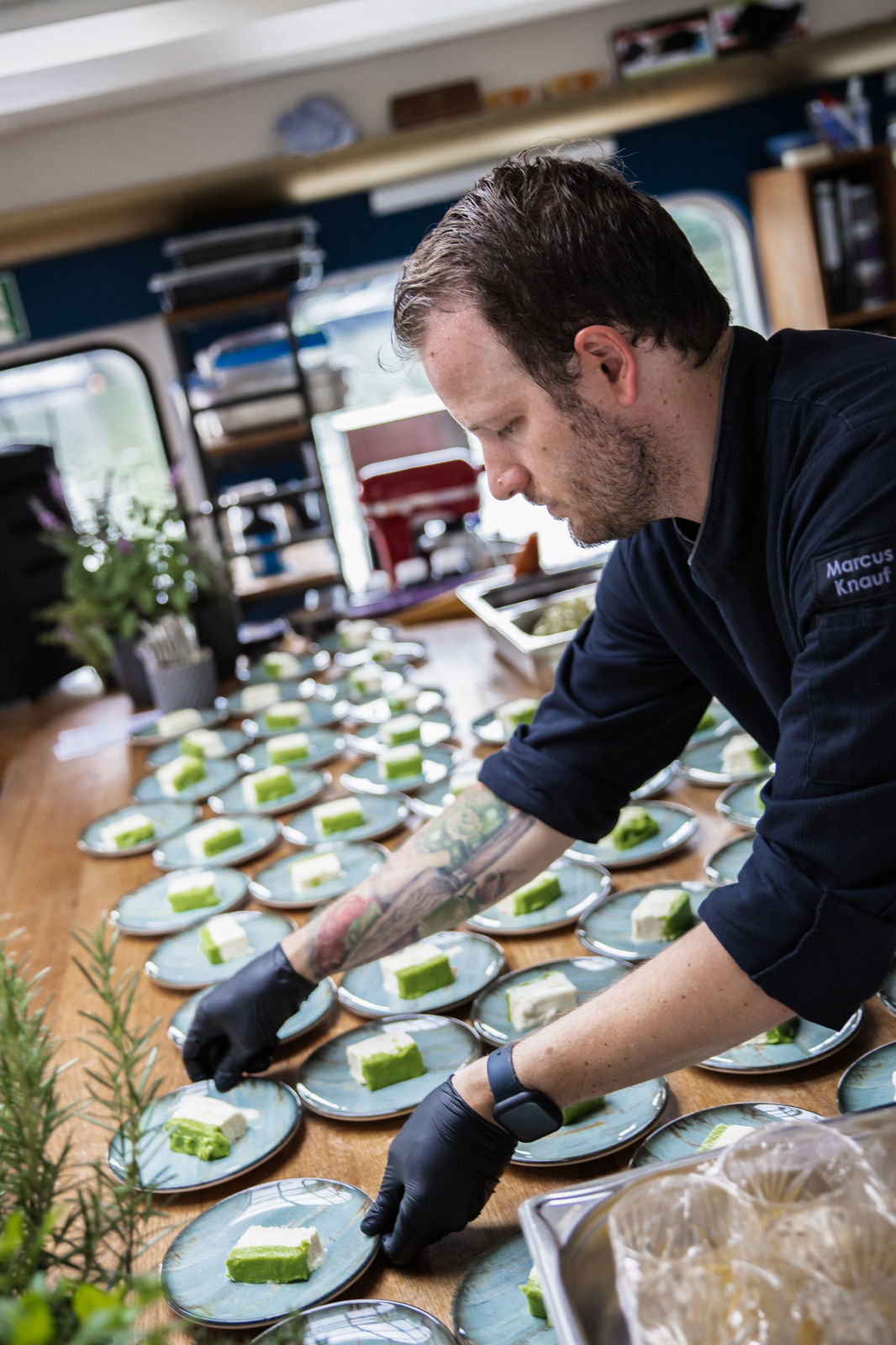 Person with short bob haircut wearing a white pleated-back shirt facing away against a dark background.