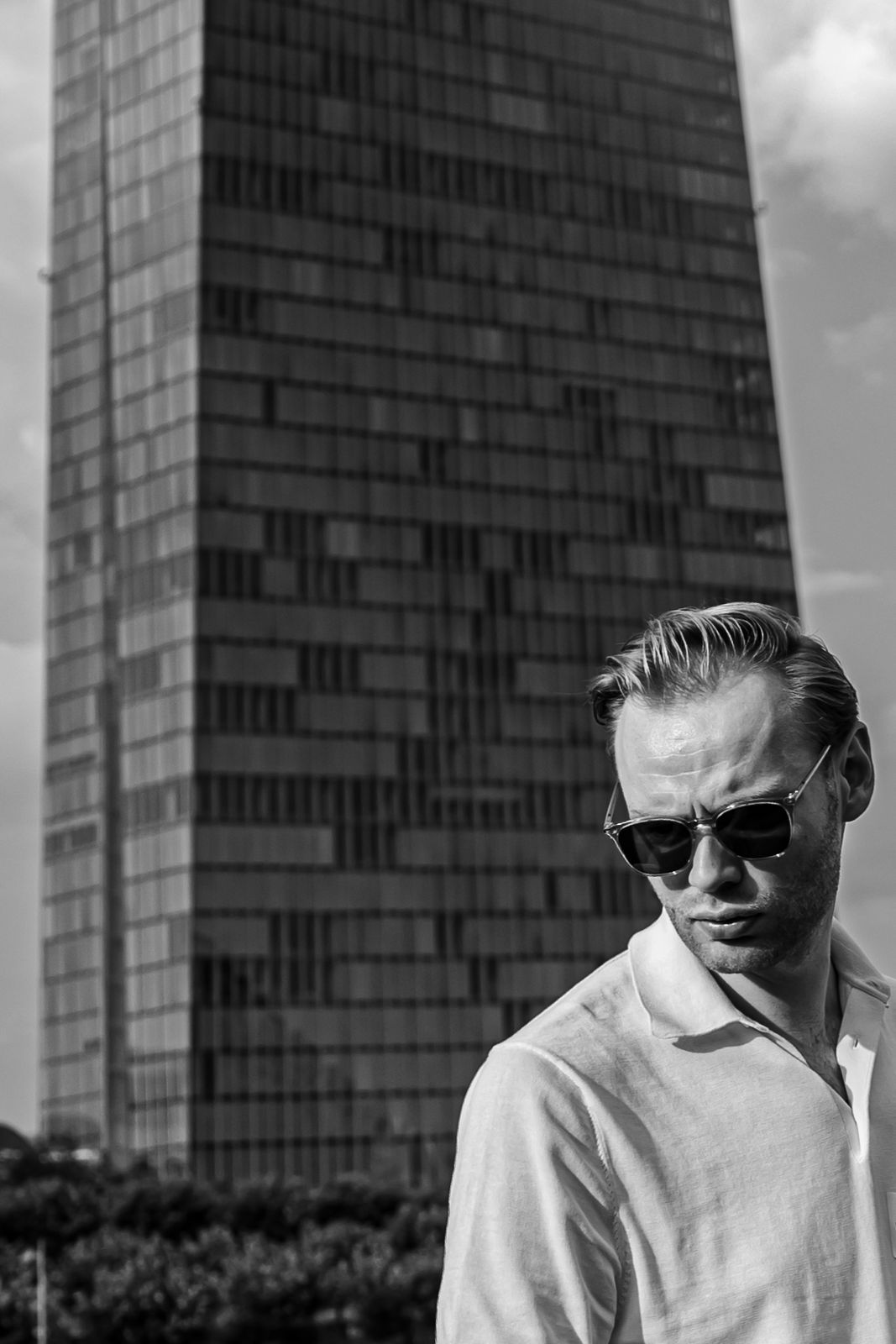 Person with short bob haircut wearing a white pleated-back shirt facing away against a dark background.
