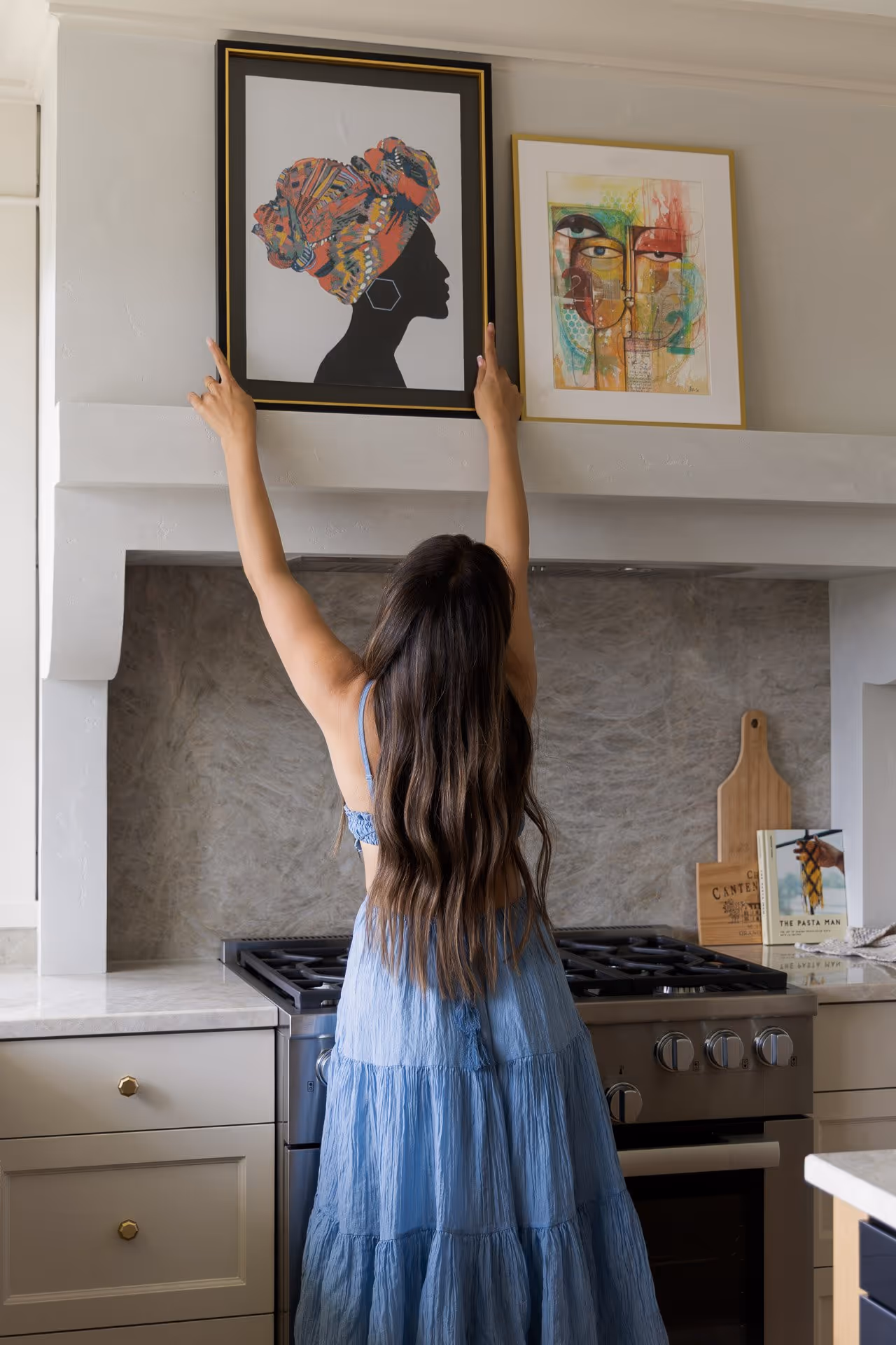 Woman arranging artwork above kitchen stove, lifestyle moment in modern kitchen interior photography