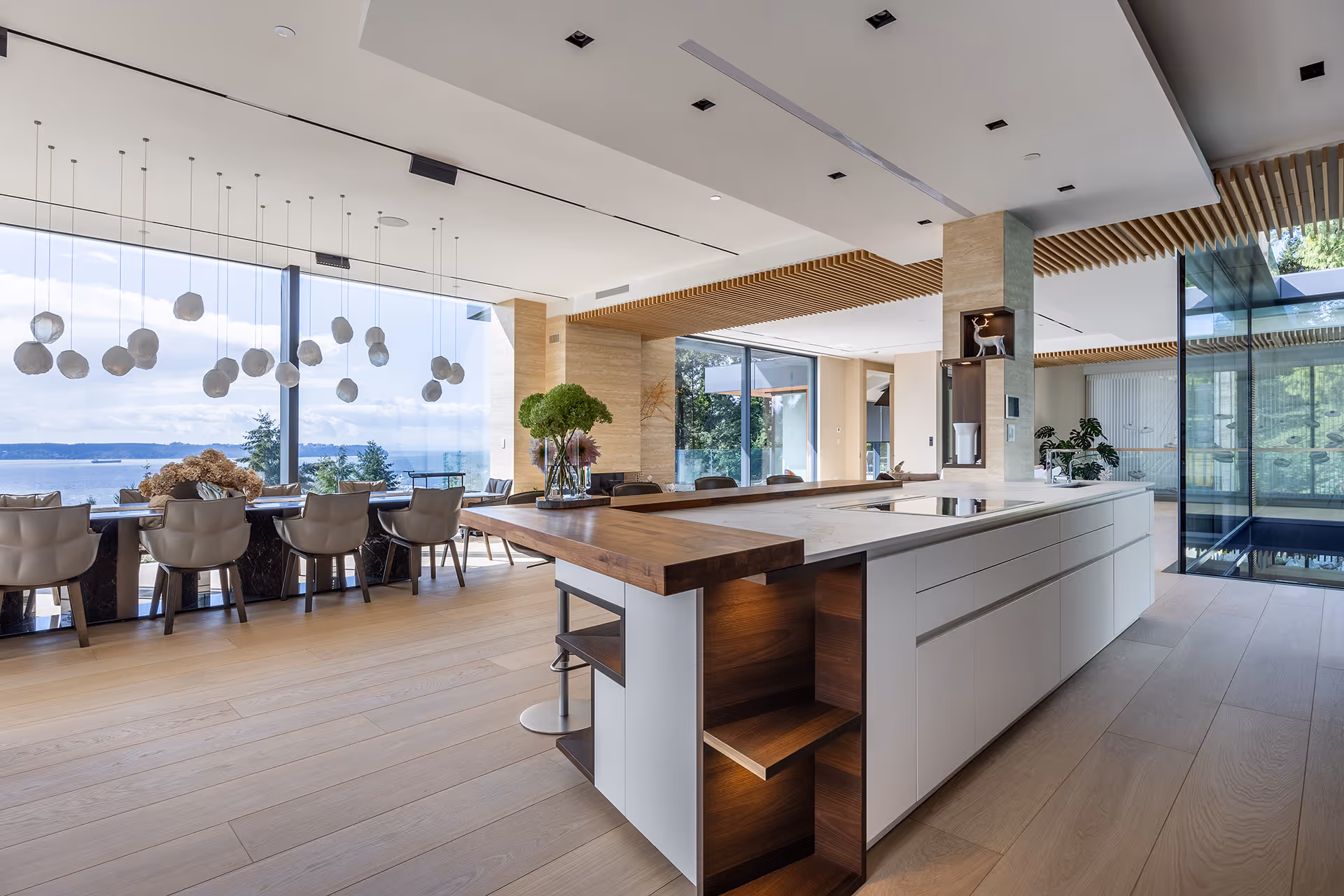 Spacious modern kitchen and dining area with large island, wood accents, and floor-to-ceiling windows, residential interior photography