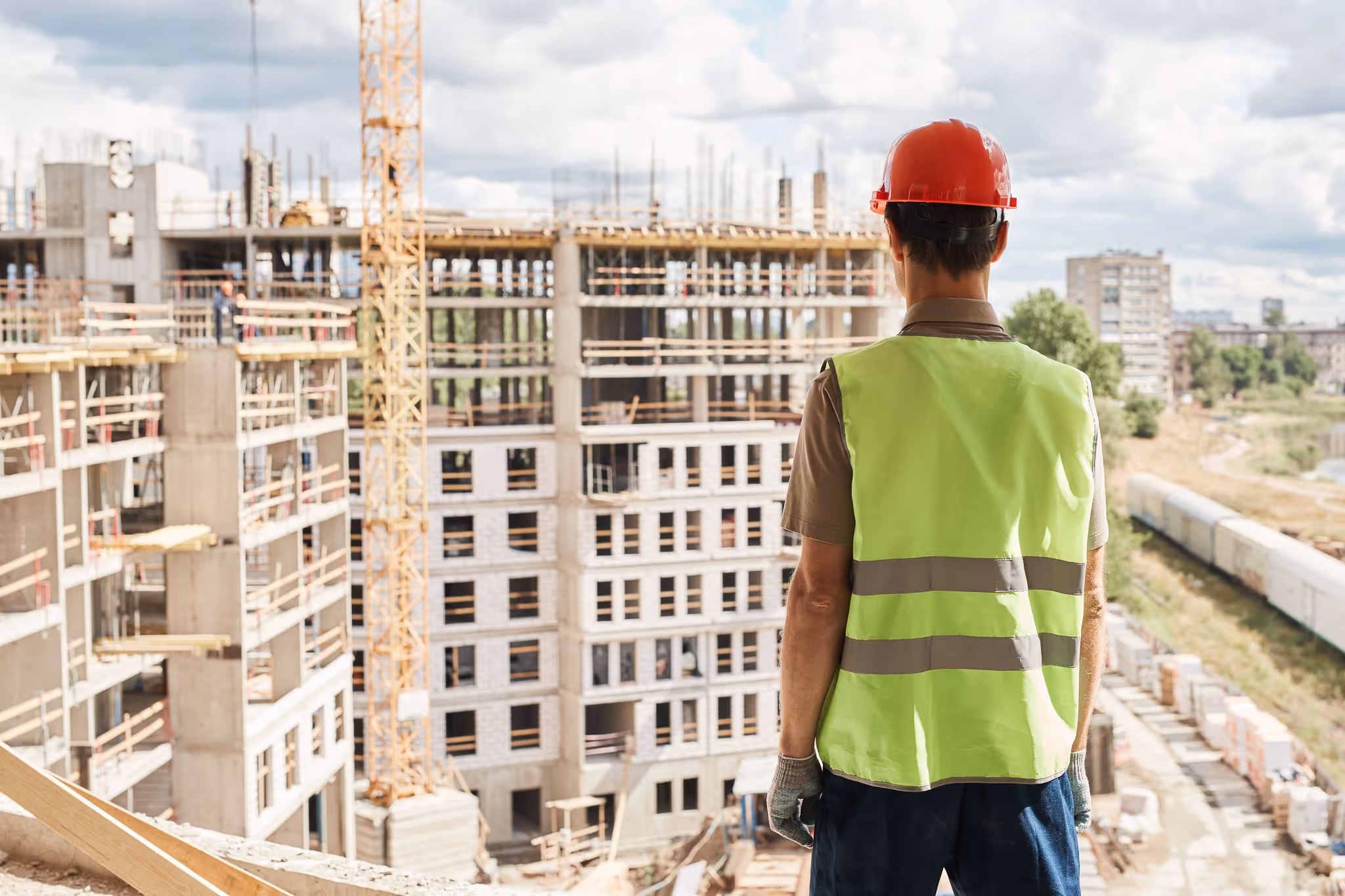 Construction worker in safety vest overlooking building site, urban development and construction photography