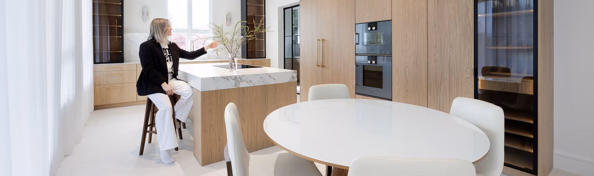 Modern kitchen and dining area with marble island, wood cabinetry, round table, and natural light, Burnaby residential interior photography