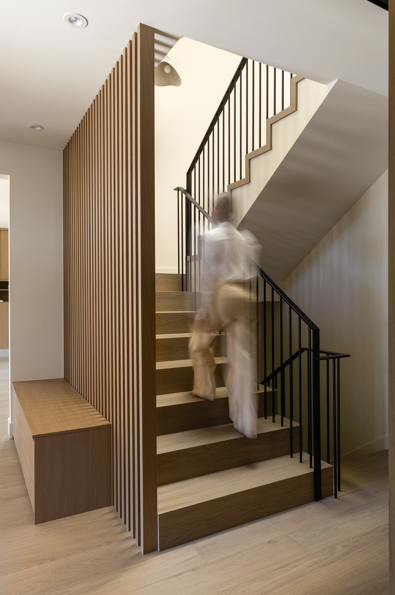 Figure in motion on The Oku House staircase beside a slatted wood wall, Vancouver interior