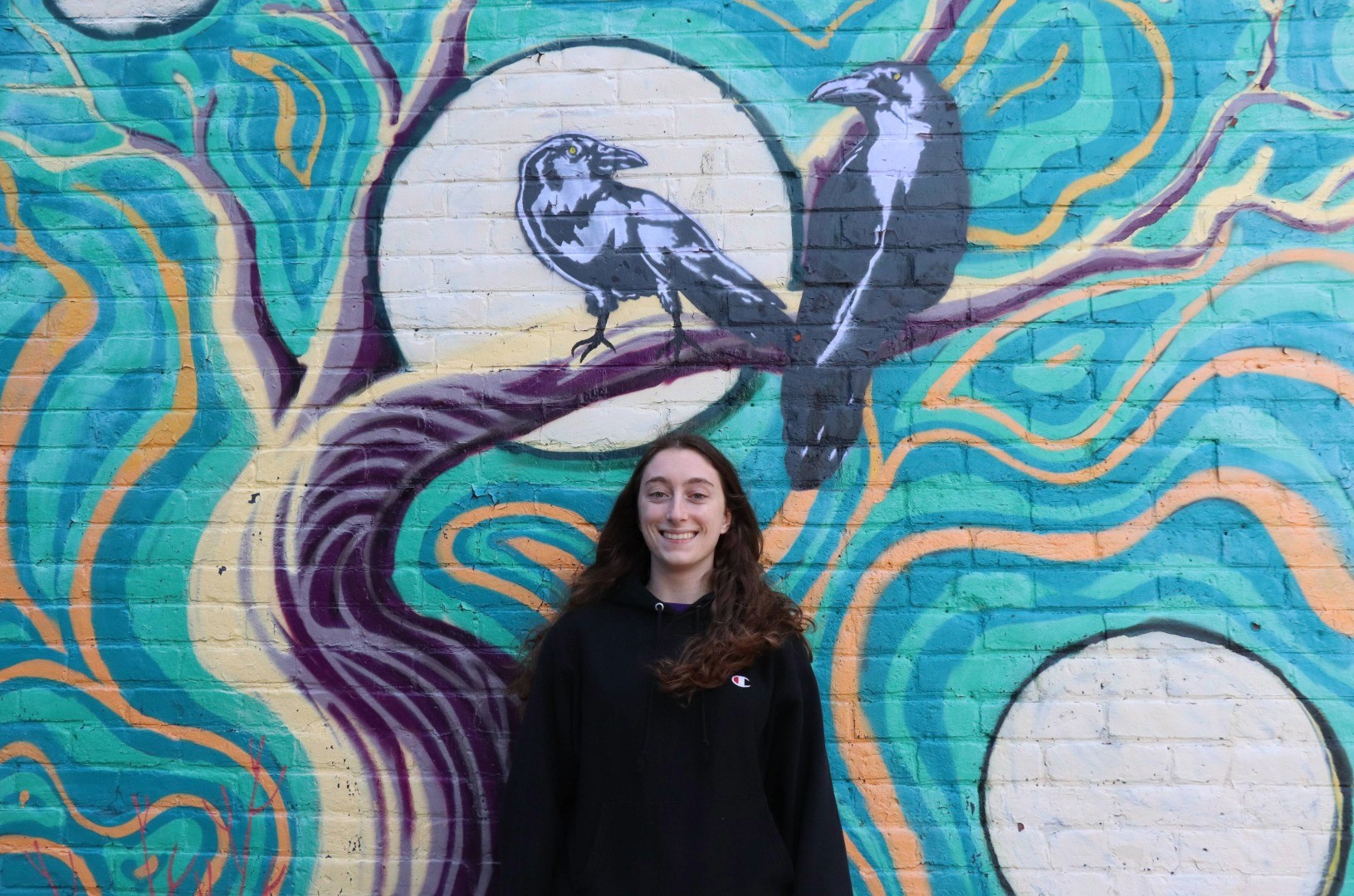 Photo of Owen Smith holding is camera in front of a mural with two crows.