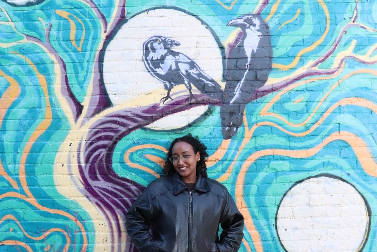 Photo of Habone Omar Hassan in front of a mural with two crows.