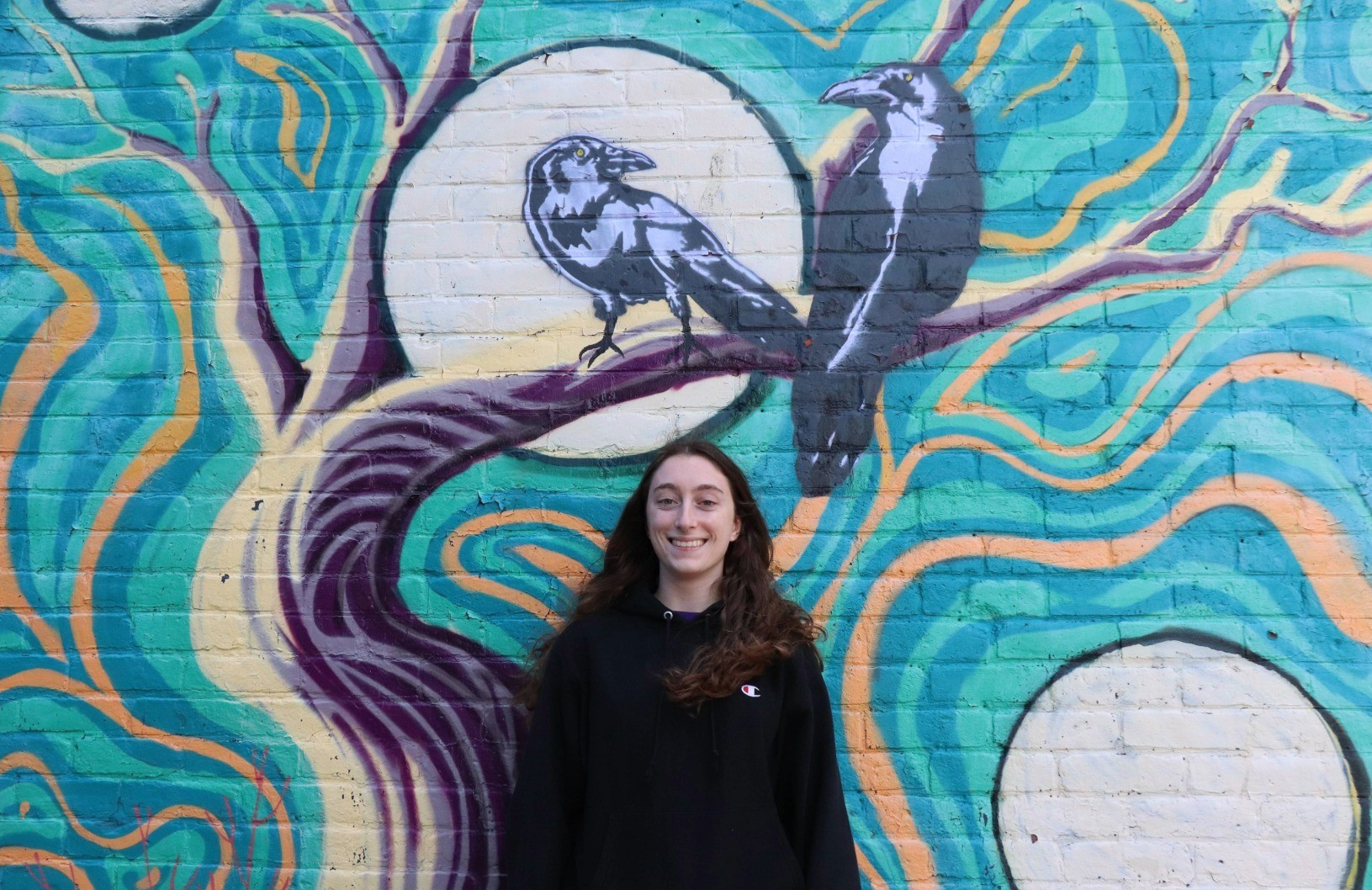 Photo of Alicia Primiani in front of a mural with two crows.