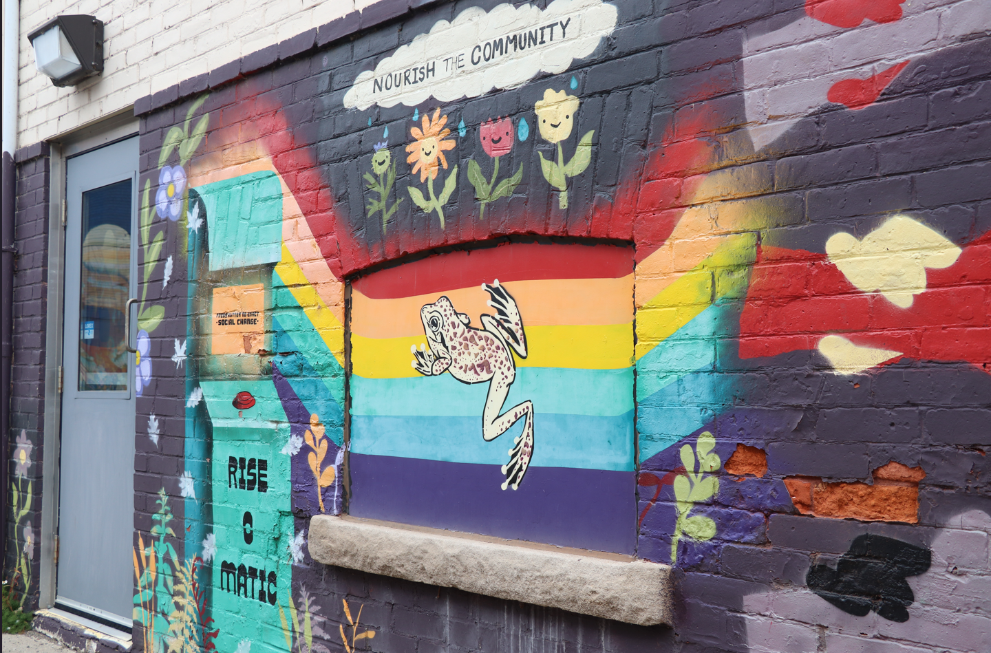 Photo os a rainbow mural with a frog, flowers, and phrase "Nourise the Community"