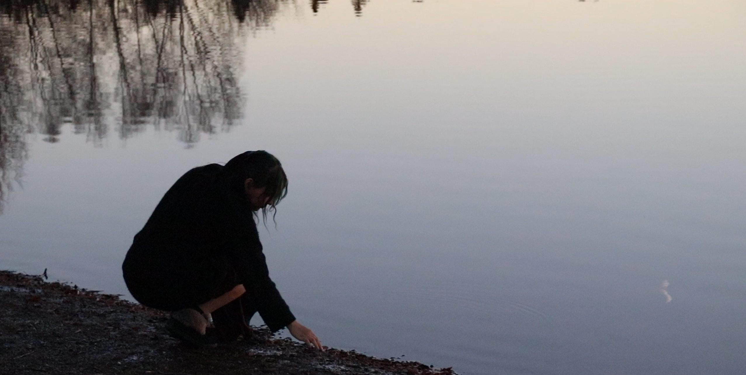 Photo of Kayleigh Legarde reaching down to touch the water of a lake
