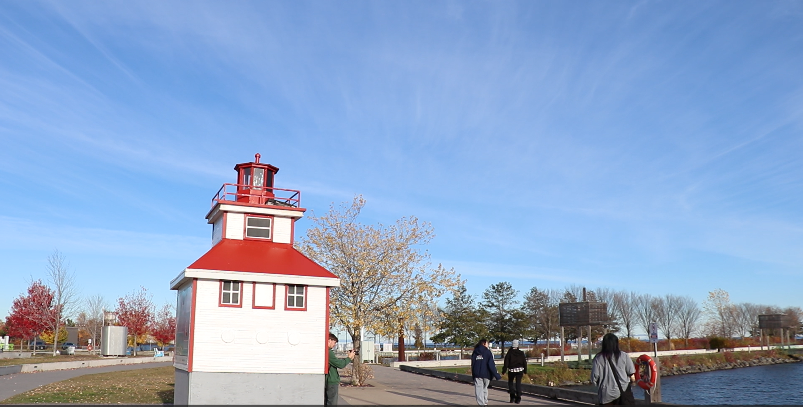 Photo of a group walking near the water with a red and white building to the left