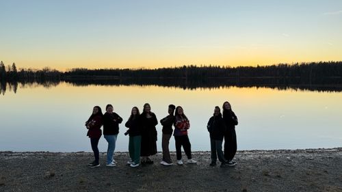 Photo of Indigenous youth and Carleton students in front of the lake at sunset