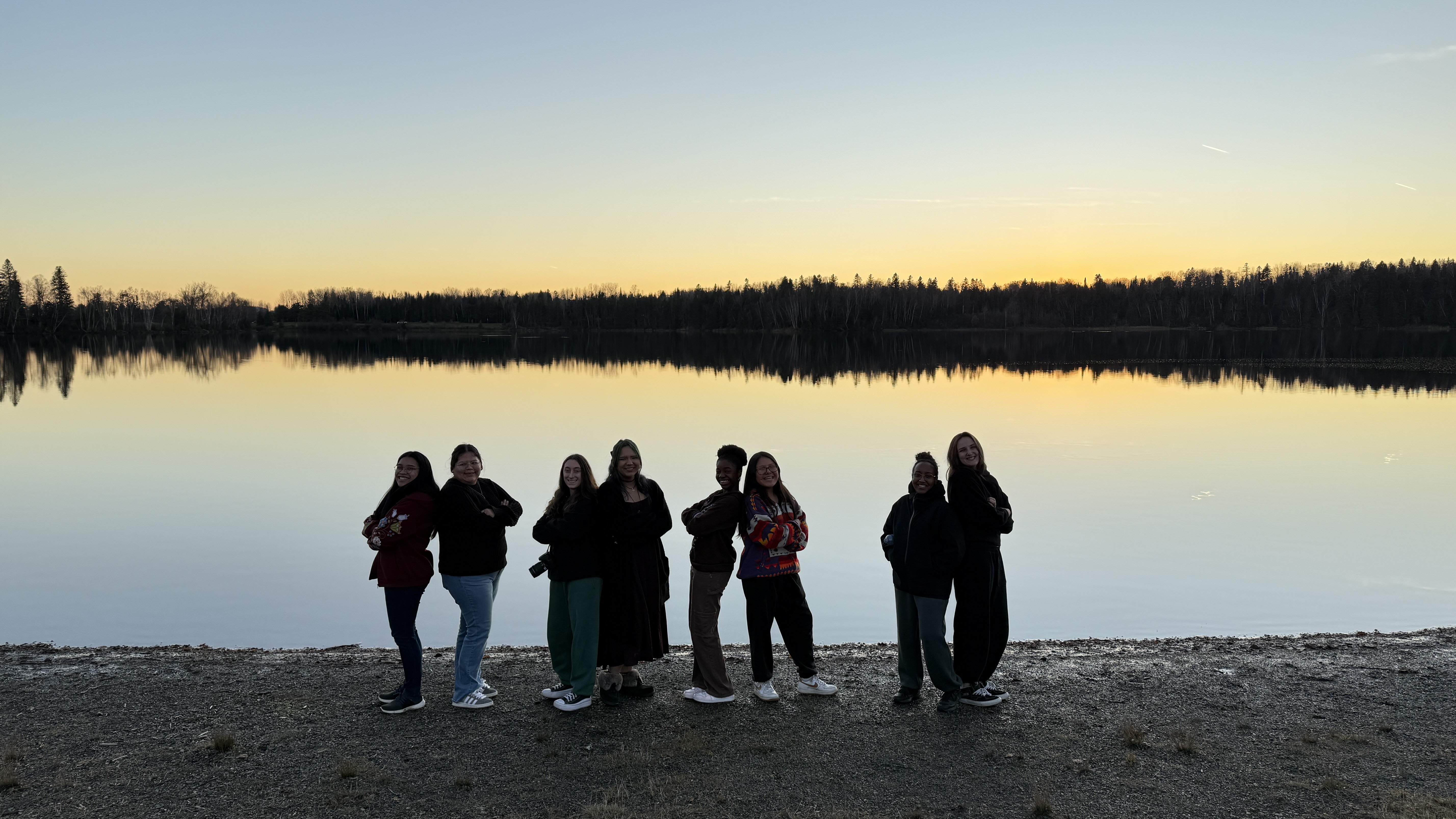 Photo of Indigenous youth and Carleton students in front of the lake at sunset