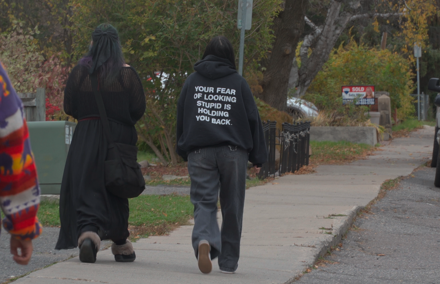Photo of two youth walking together, with one of their sweaters saying "your fear of looking stupid is holding you back"
