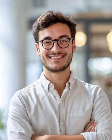 Smiling man with glasses in a bright, modern indoor background.