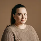 Portrait of a woman smiling softly in beige sweater with neutral backdrop.