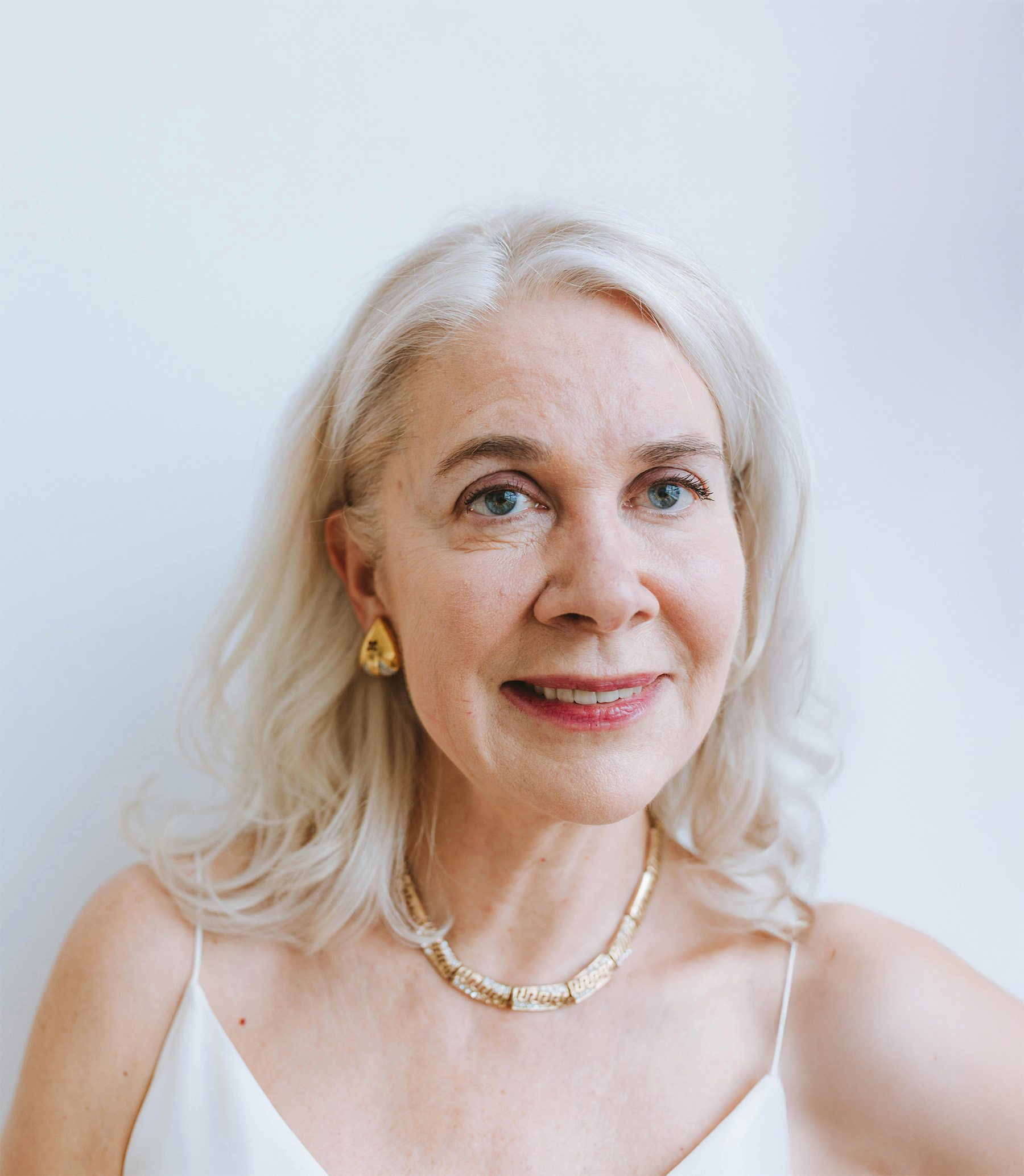 Smiling woman with long brown hair wearing a dark purple wide-brimmed hat against a muted purple background.