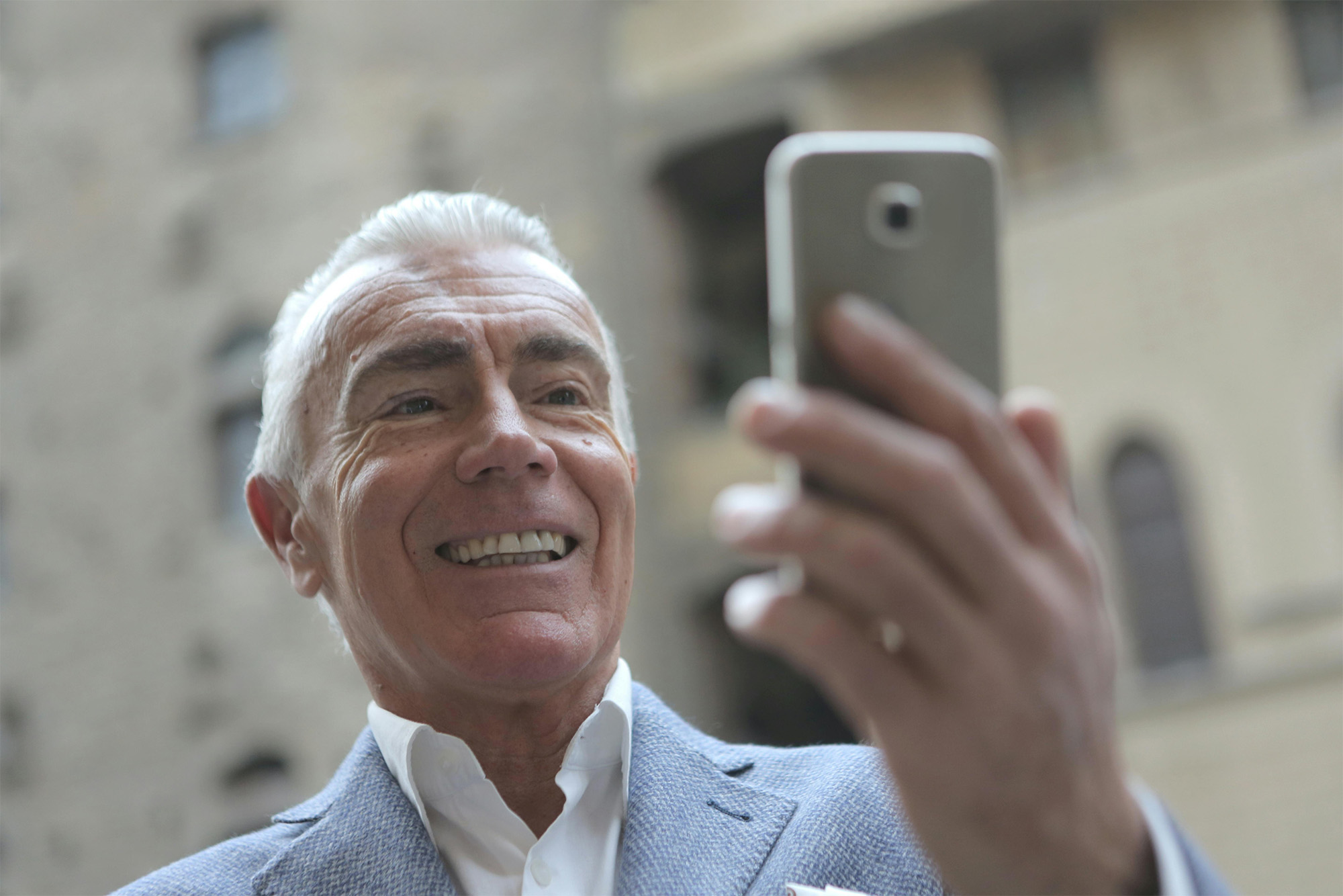 Smiling woman with wavy blonde hair holding a hand mirror, examining her teeth.