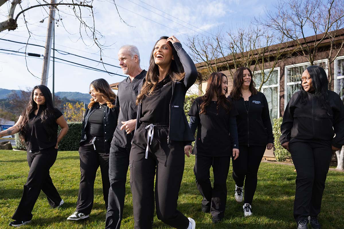 Group of seven diverse healthcare professionals smiling and walking outside on grass near a building.