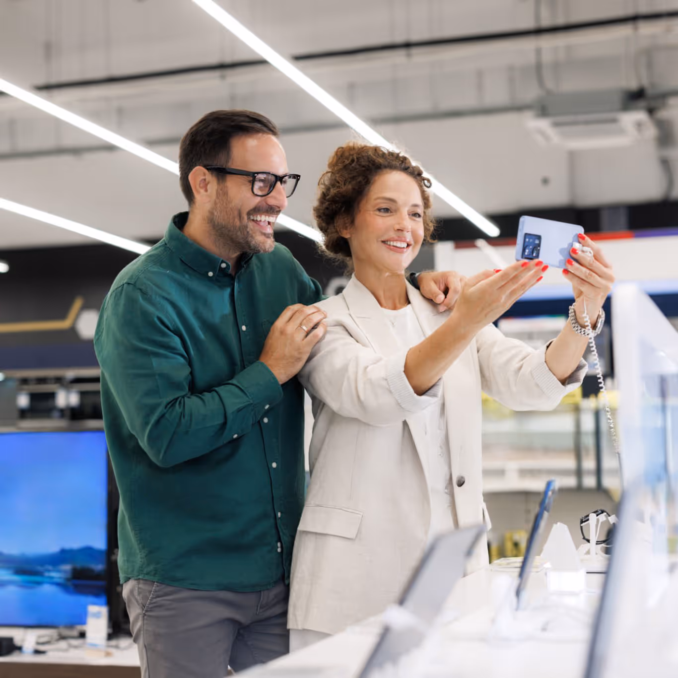 Smiling couple in an electronics store looking at and holding a smartphone on display.