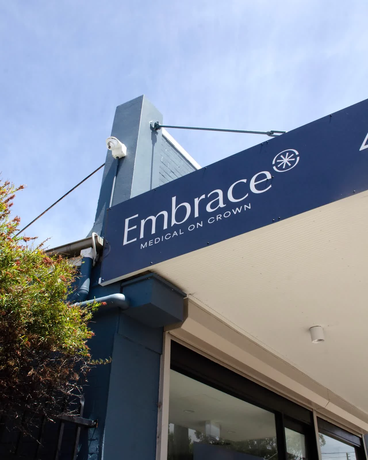 Blue building corner with a sign reading 'Embrace Medical on Crown' under a clear sky.