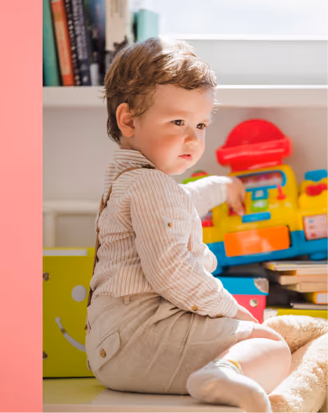 Young child sitting on the floor near colorful toys, looking to the side.