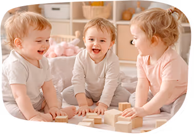 Three toddlers sitting on the floor playing with wooden building blocks, smiling and interacting.
