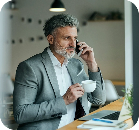 Meydan FZ businessman in gray suit talking on phone, drinking coffee at decorated desk