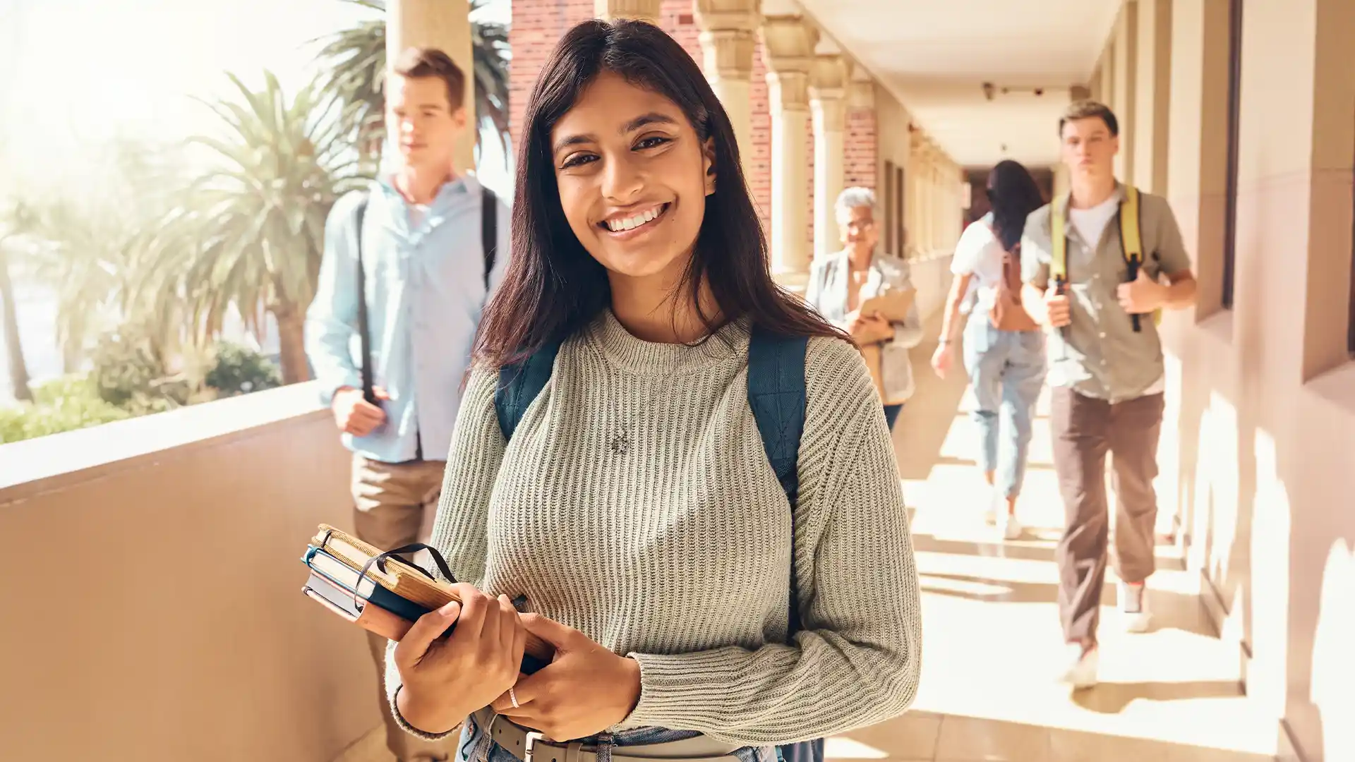 Indian student in Dubai smiling while looking at the camera and holding books in school hallway