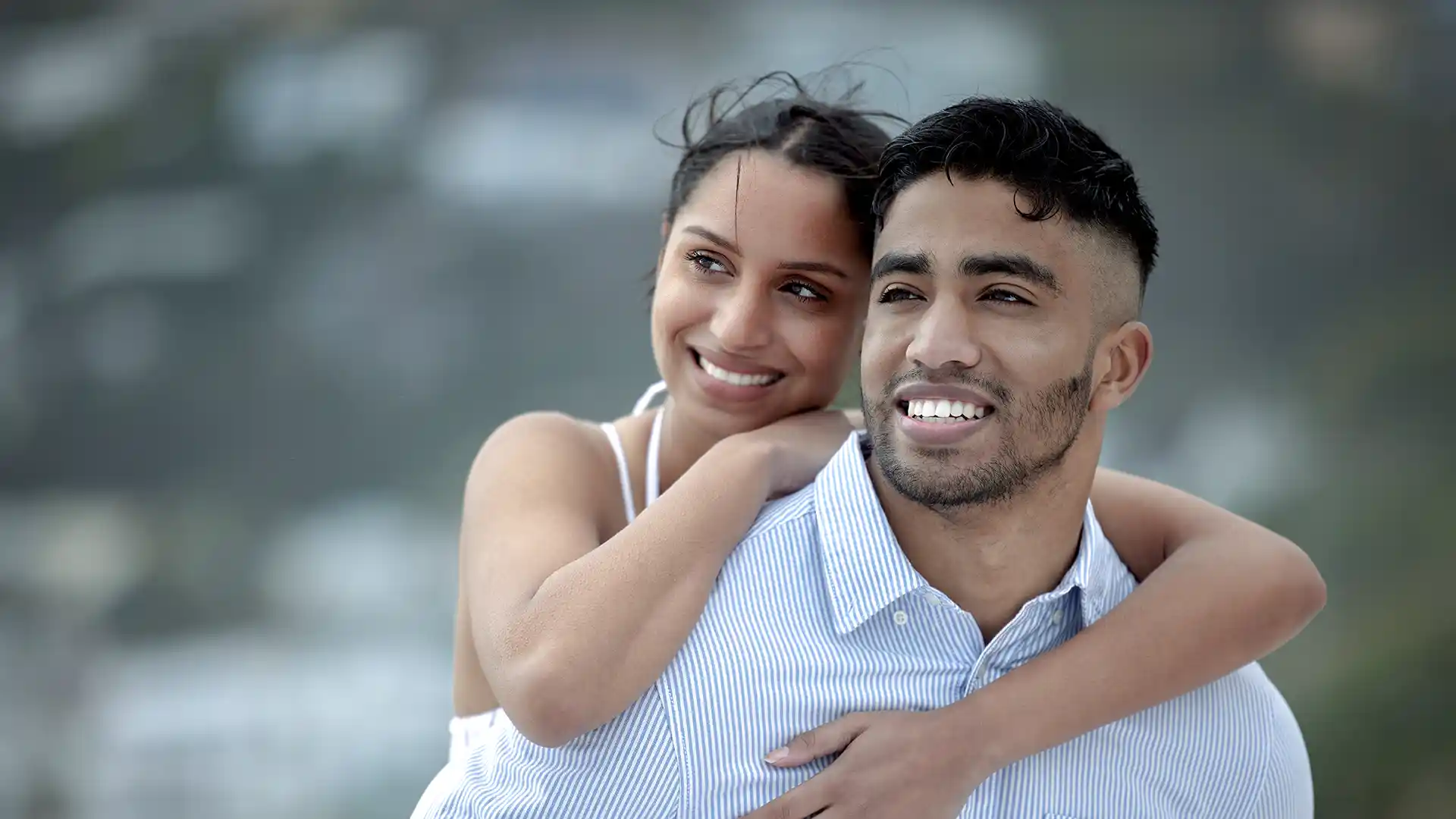 A young, happy couple outdoors, with the man giving the woman a piggyback ride.