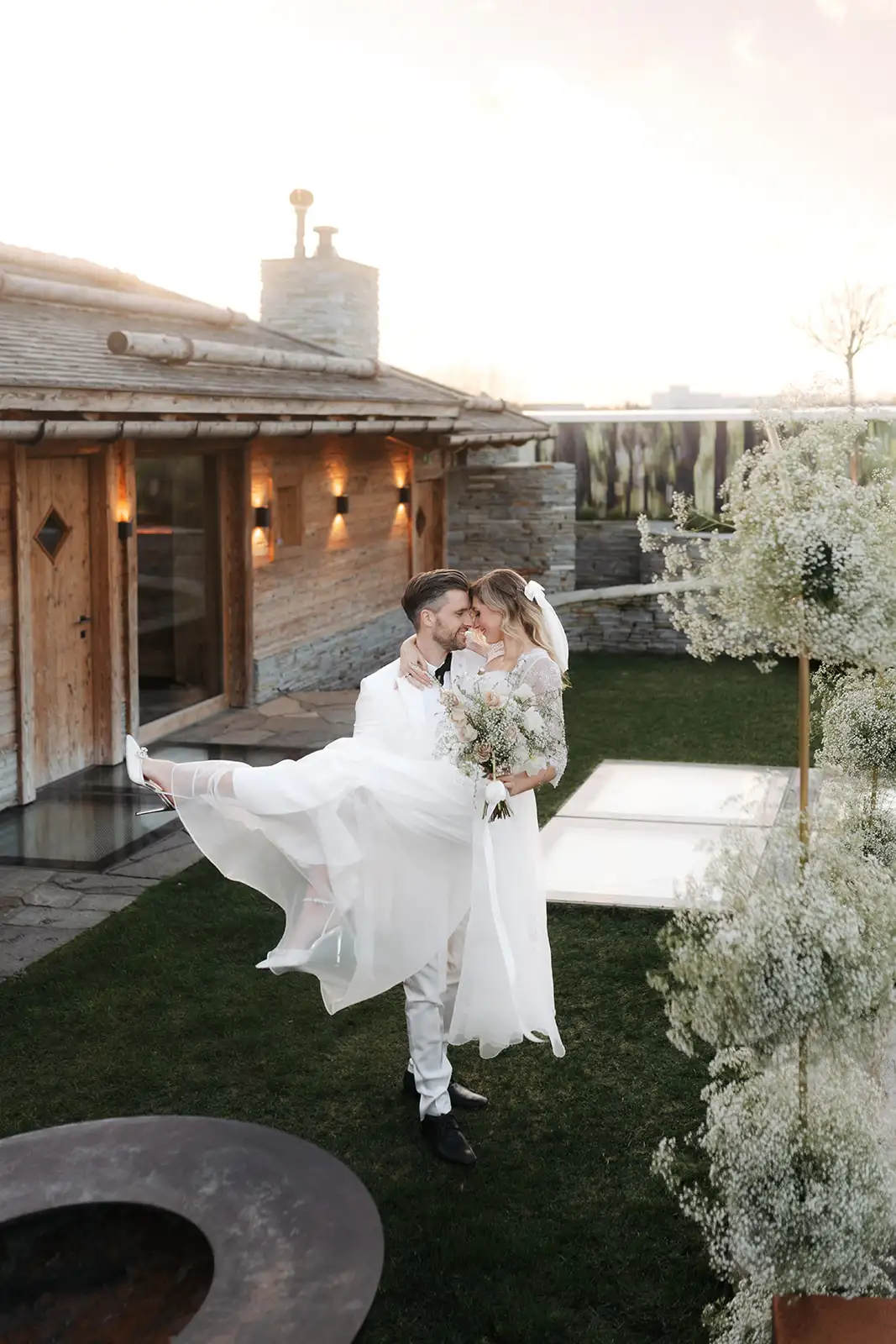 Hochzeit Paarshooting Paar vor dem Chalet draußen, Braut wird getragen vom Mann