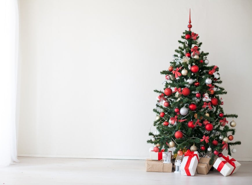 A large Christmas tree decorated in red, white and gold, in a white room, surrounded by piles of red and white wrapped Christmas presents.