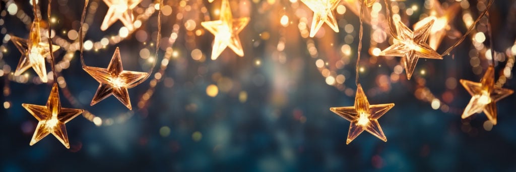 A festoon of gold star Christmas decorations against a navy blue backdrop.