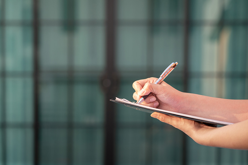 a pair of hands writing on a clipboard with a pen