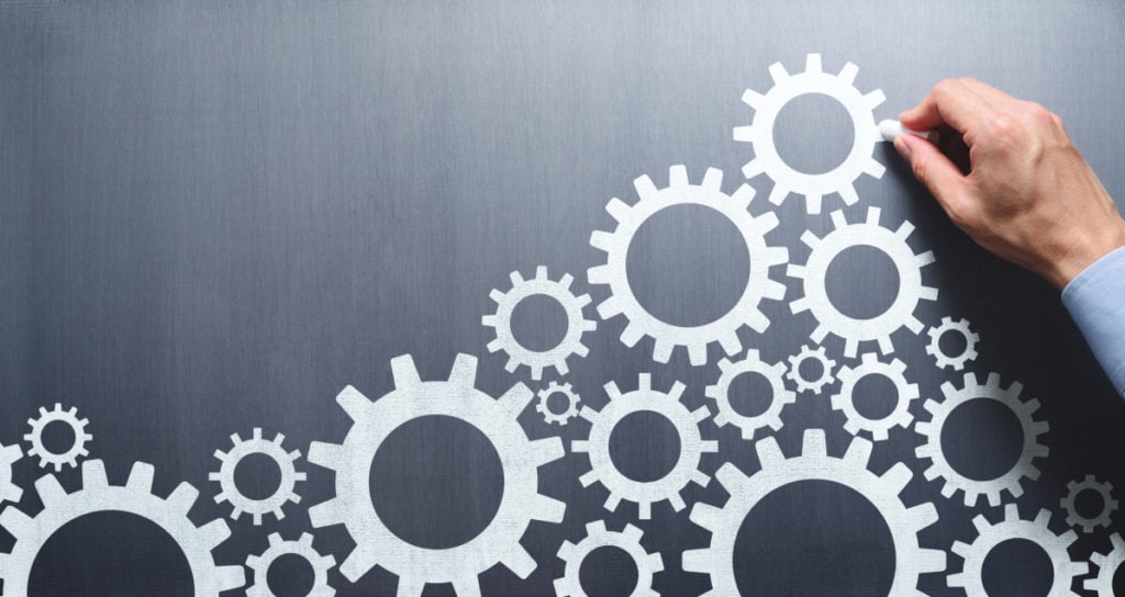 a male hand drawing interwoven cogs on a blackboard