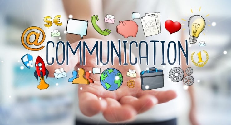 A man’s hand holding a cartoon graphic of the word COMMUNICATION surrounded by related business symbols such as a lightbulb, cogs, a telephone handset and a briefcase. 