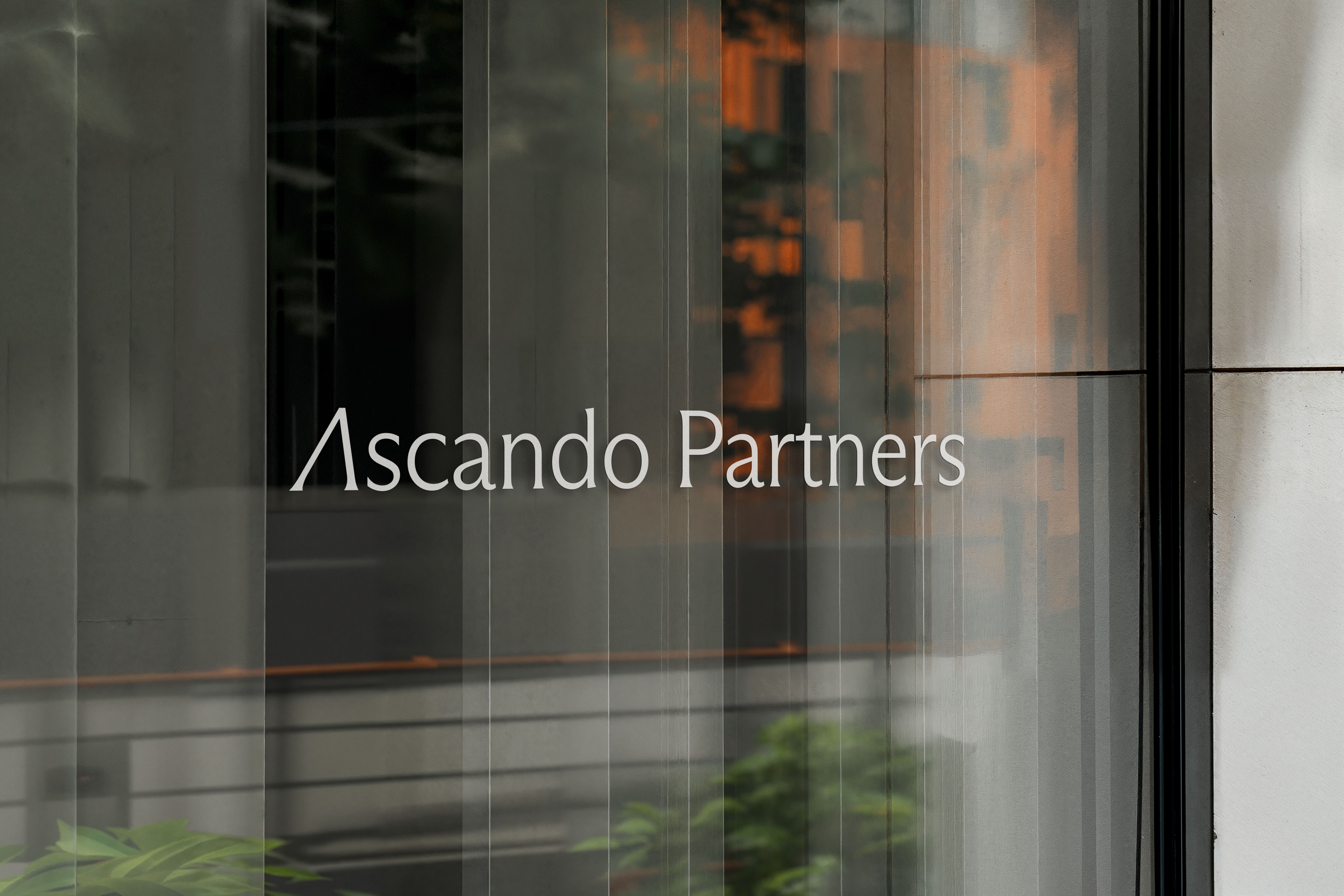 Glass window with the text 'Ascando Partners' and blurred reflections of buildings and greenery.