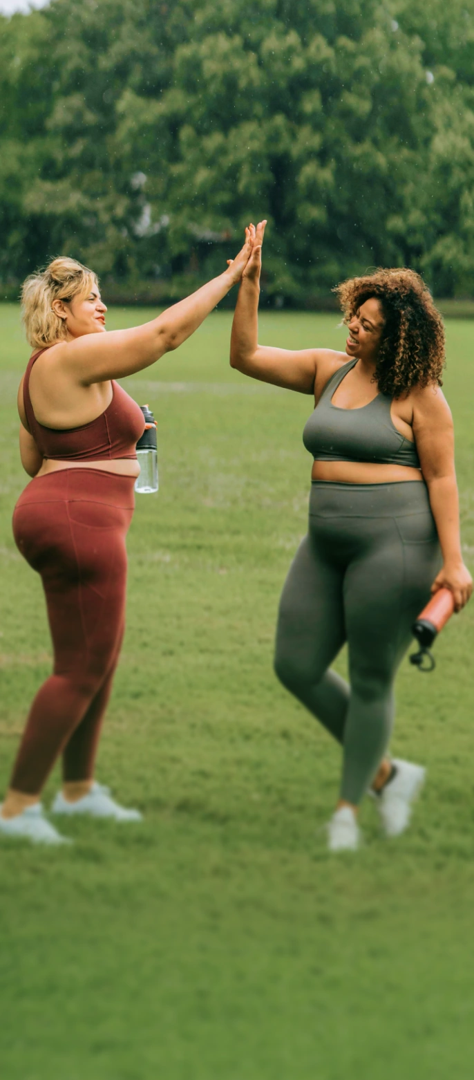 Two women high-fiving outdoors, representing clinically guided weight loss care