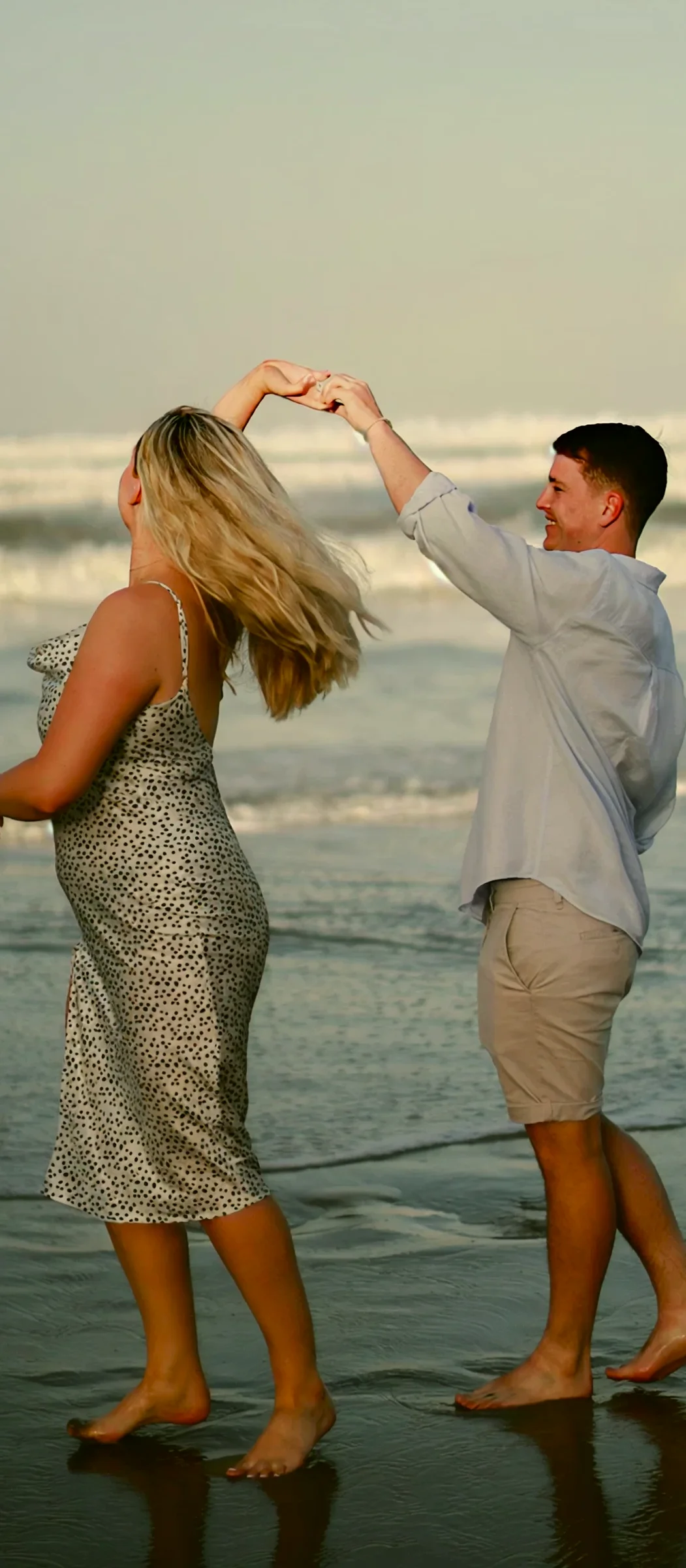 Couple dancing on a beach at sunset, hands raised as she spins