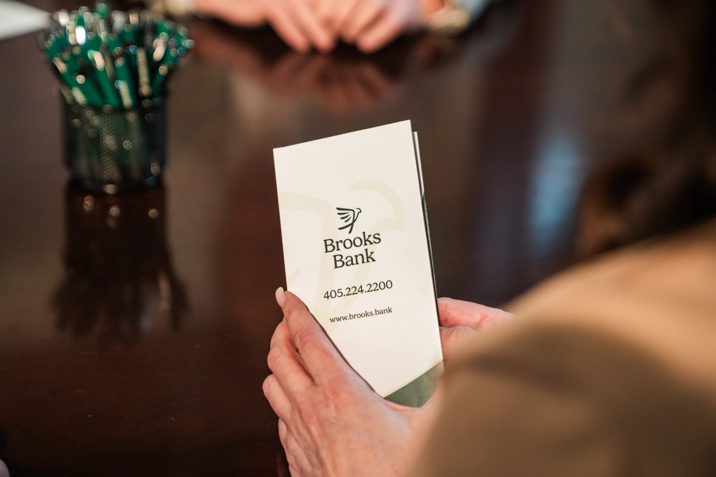 Customer holding a Brooks Bank business card at the teller counter