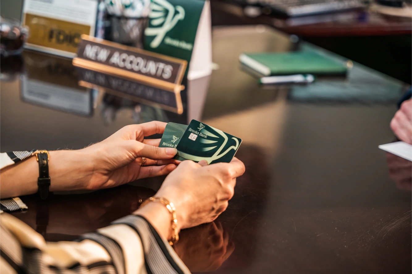 Customer holding two Brooks Bank cards at the new accounts desk