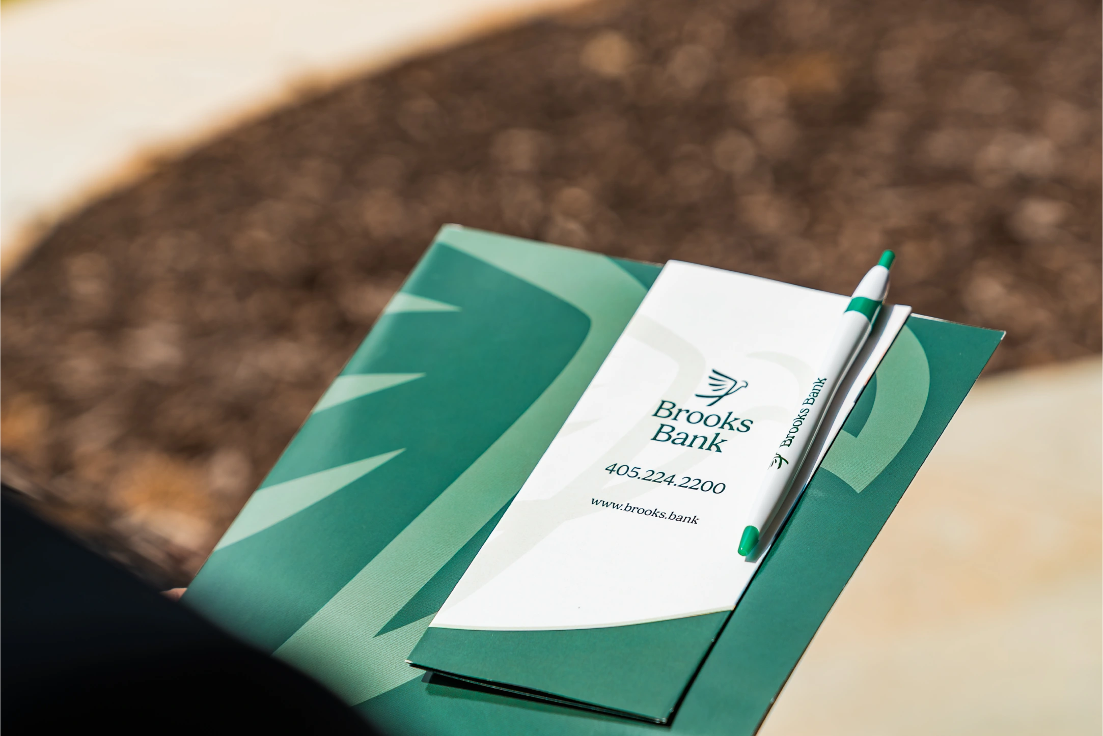 Brooks Bank folder, brochure and branded pen held outdoors