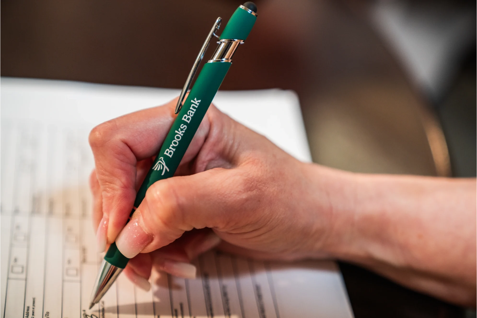 Hand filling out a Brooks Bank form with a branded pen