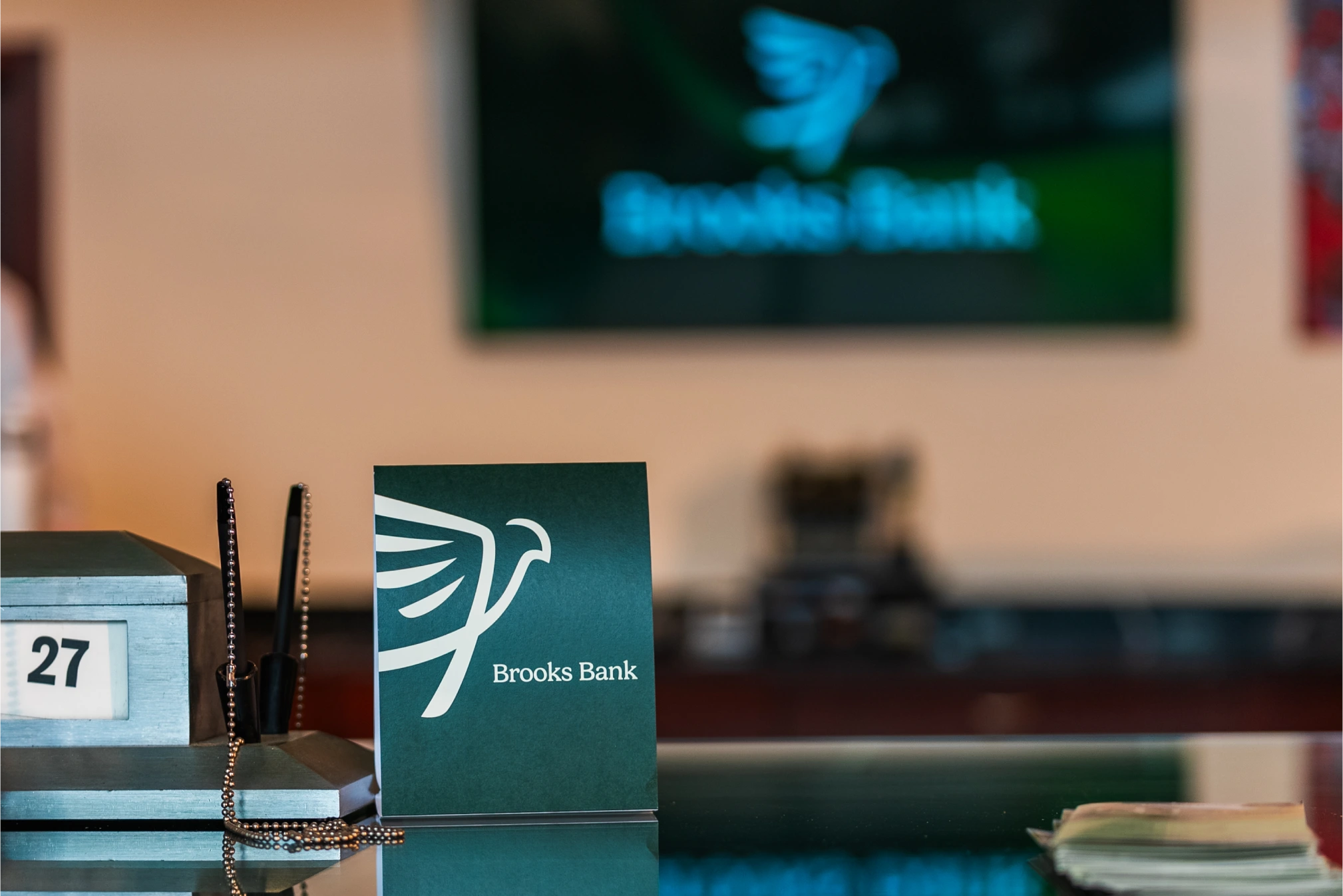 Brooks Bank tent card on a teller counter under the bank's logo screen