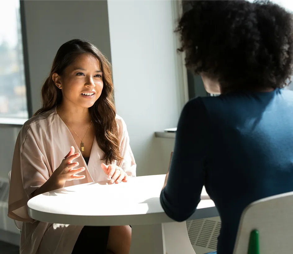 Two women discuss Bildung and Weiterbildung at a table in a Bildungsakademie setting.