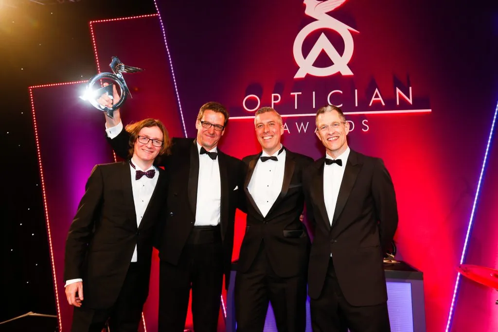 Four men in tuxedos smiling and posing together at the Optician Awards event, one holding a trophy.