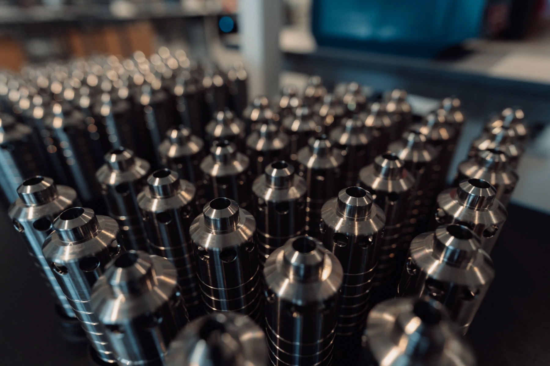 Rows of cylindrical metal components with polished tops arranged closely together on a dark surface.