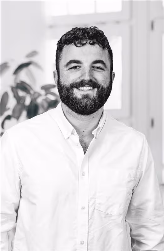 Porträt eines lächelnden Mannes mit dunklem lockigem Haar und Bart, der ein weißes Hemd trägt.
