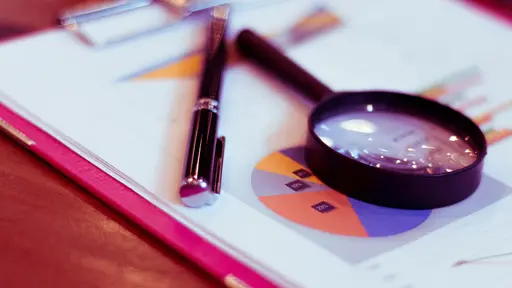 Black pen and magnifying glass resting on a financial report with colorful pie charts.