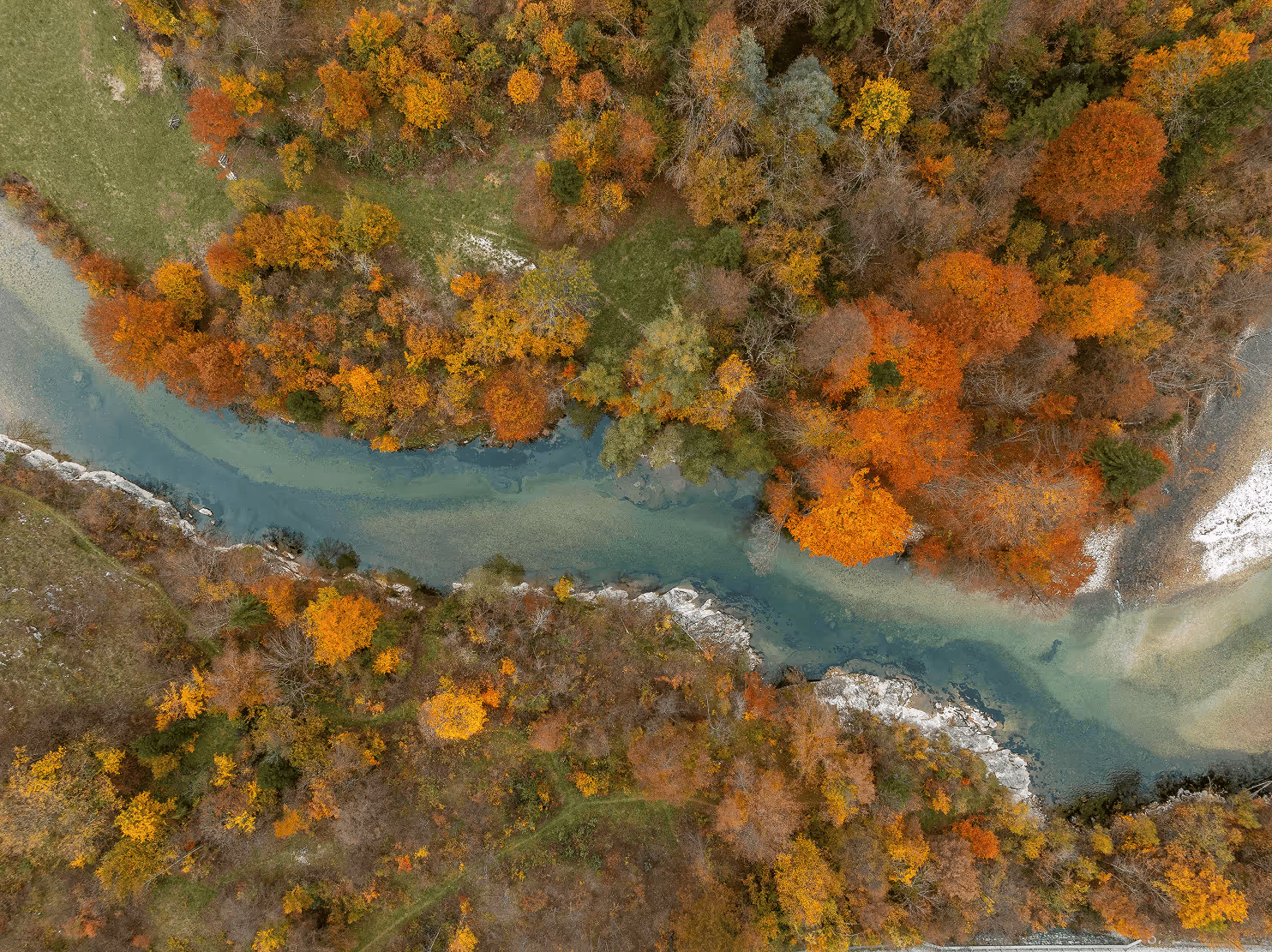 Aerial view of a winding river surrounded by a forest with autumn foliage in shades of orange, yellow, and green.
