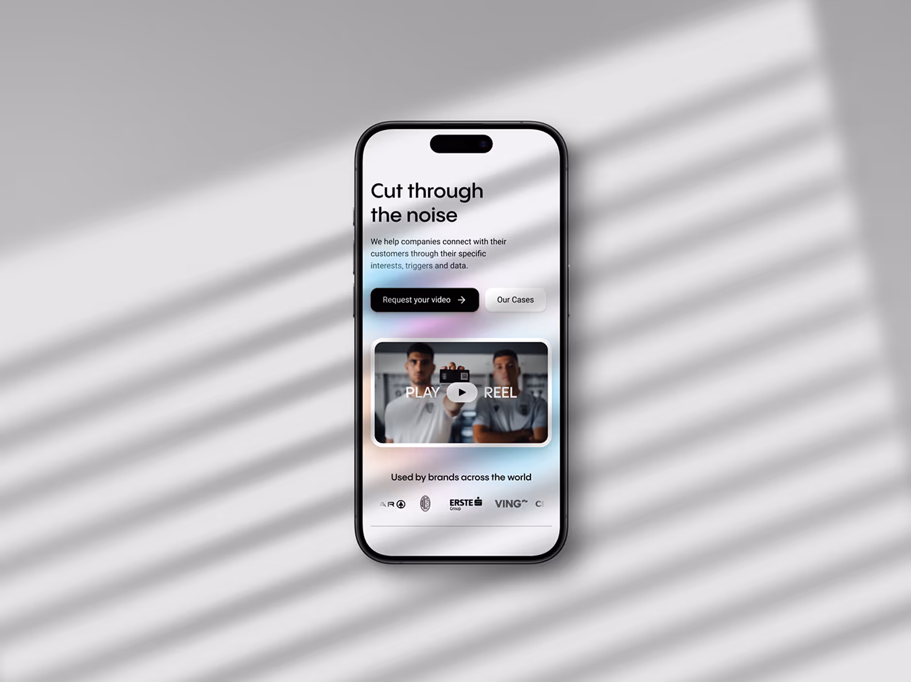 Smartphone displaying a webpage with text 'Cut through the noise', buttons labeled 'Request your video' and 'Our Cases', a video thumbnail showing two men, and brand logos at the bottom.